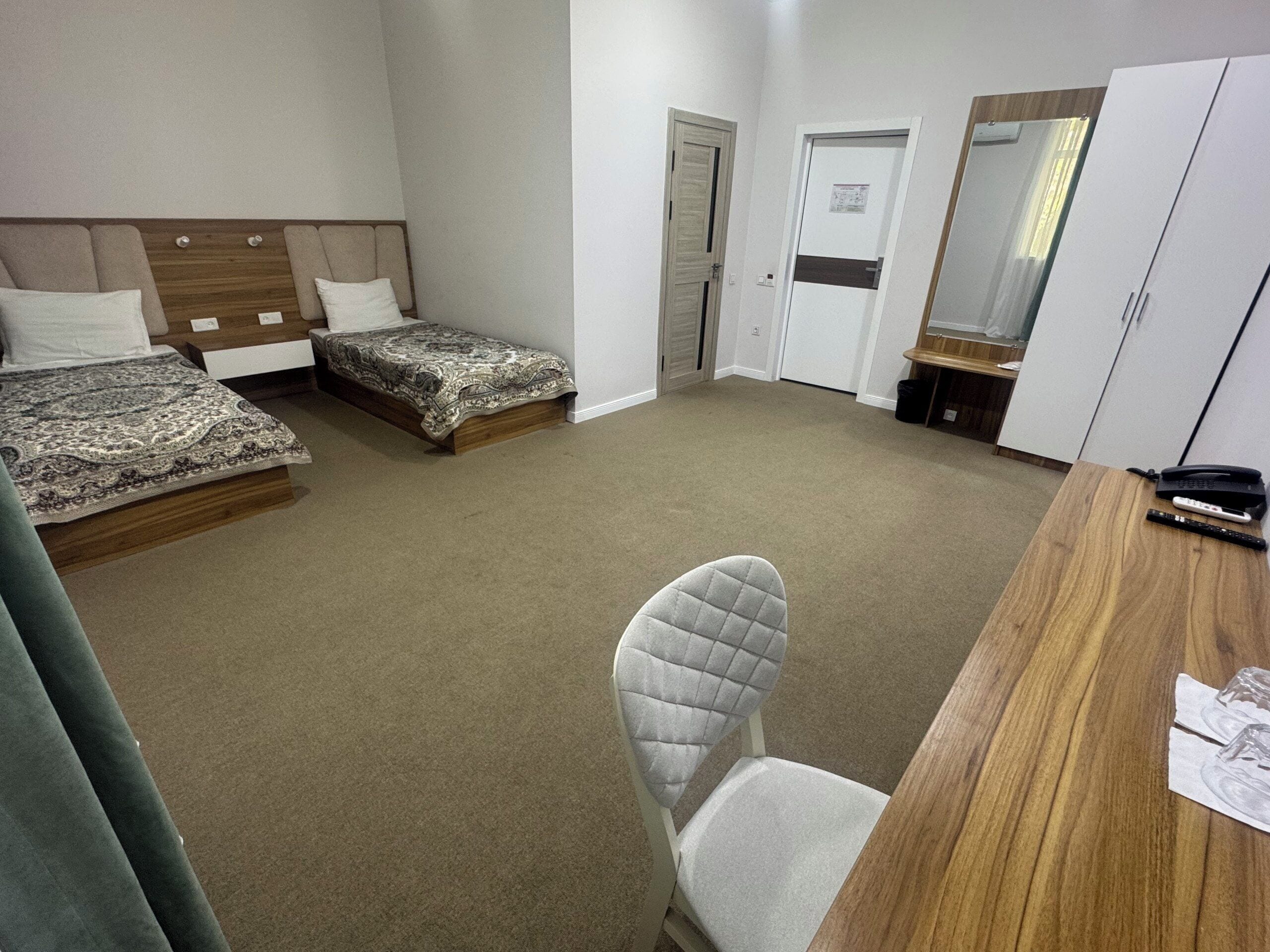 A hotel room with two beds, a desk, a chair, and a wardrobe.