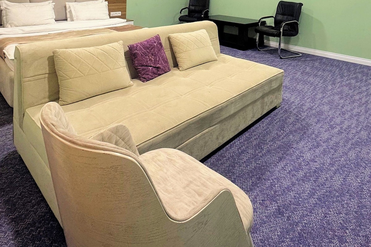 Una habitación de hotel con cama, sofá, dos sillones, escritorio y piso alfombrado.