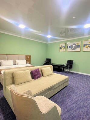 Una habitación de hotel con cama, sofá, dos sillones, escritorio y piso alfombrado.