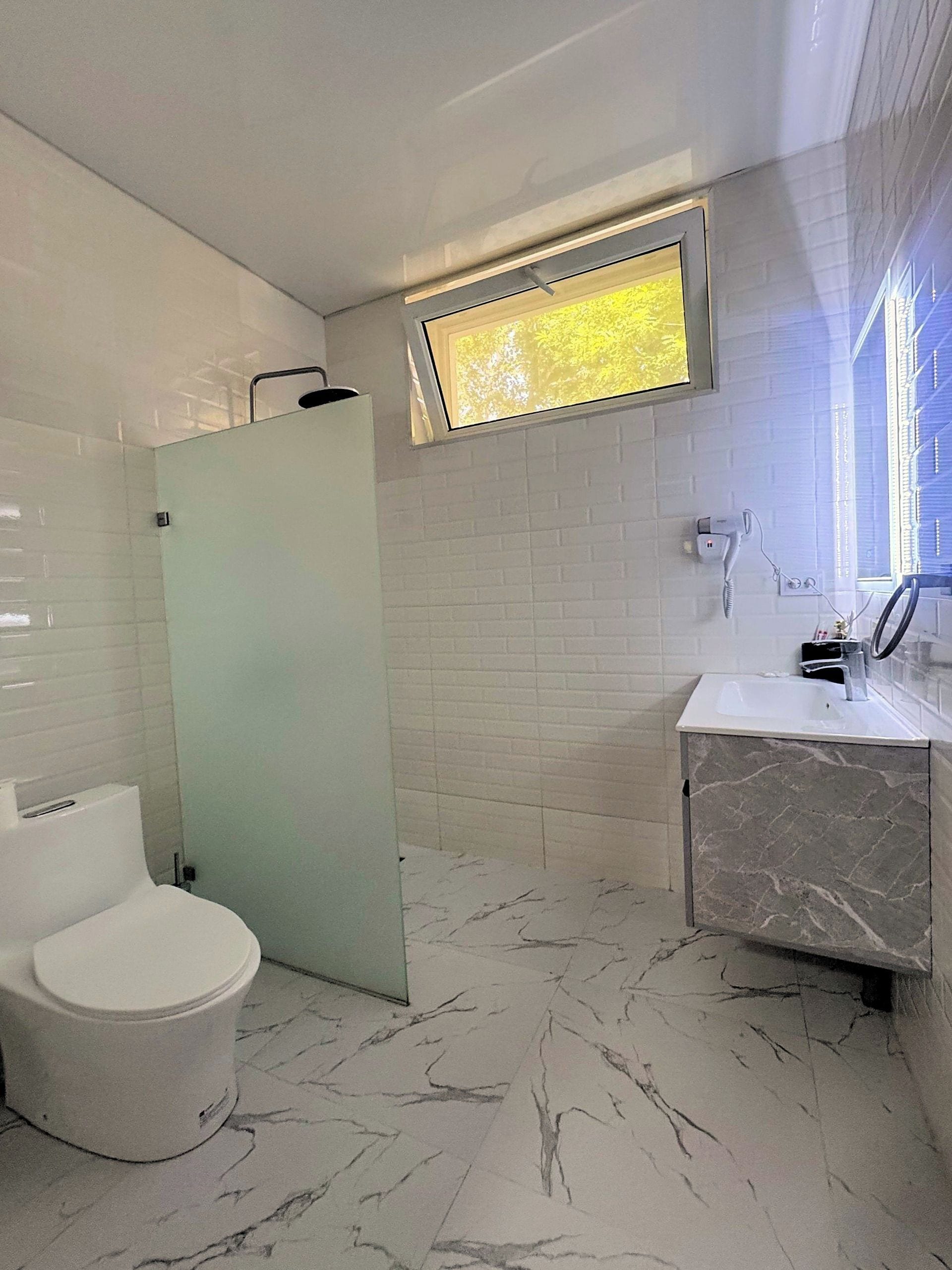Un baño con inodoro, cabina de ducha y lavamanos con encimera de mármol.