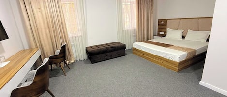 A hotel room with a bed, a desk, a chair, and a window with curtains.
