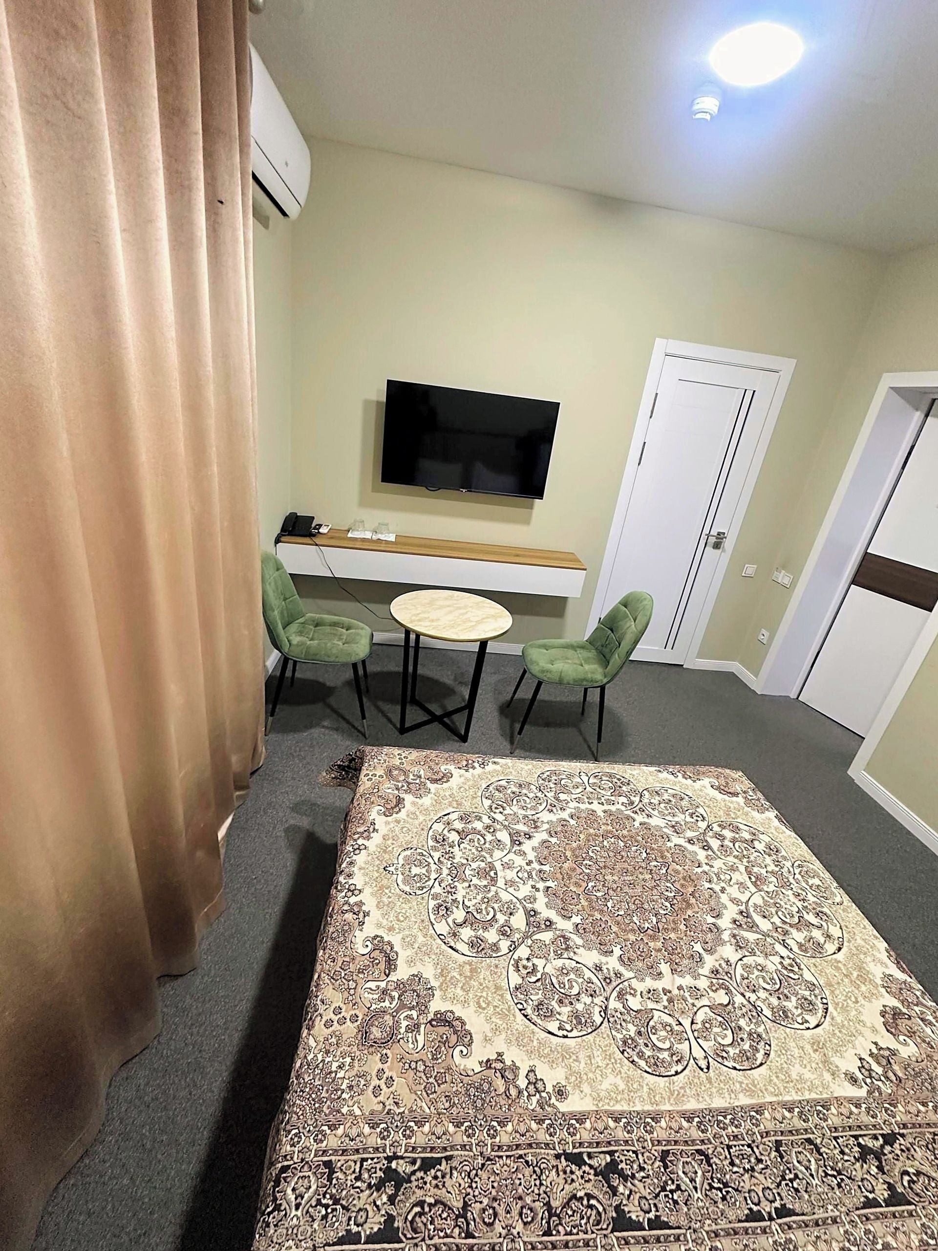 Une chambre d’hôtel avec une grande moquette à motifs, un téléviseur à écran plat fixé au mur, une petite table ronde avec des chaises et une porte dotée d’une poignée.