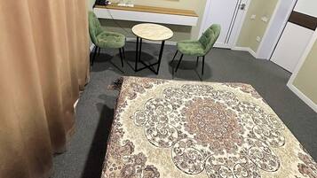 Une chambre d’hôtel avec une grande moquette à motifs, un téléviseur à écran plat fixé au mur, une petite table ronde avec des chaises et une porte dotée d’une poignée.