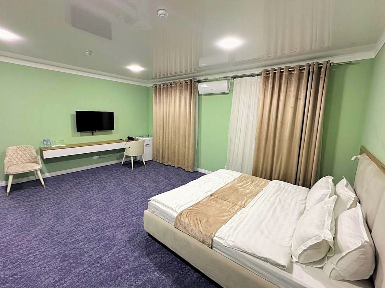 Une chambre d’hôtel avec un lit, un bureau, une chaise, une télévision et des rideaux.