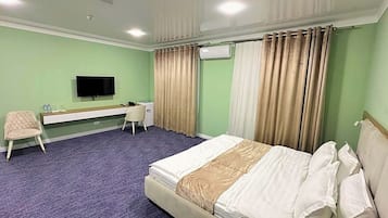 Una habitación de hotel con una cama, un escritorio, una silla, un televisor y cortinas.