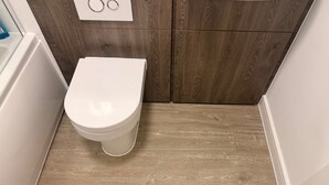A white toilet in a bathroom with a wooden floor and a white wall. - Manchester 1-bed Apartment, Sleeps 2 (Manchester)