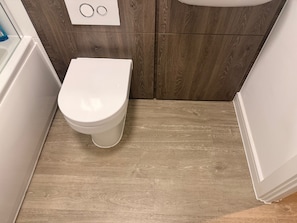 Eine weiße Toilette in einem Badezimmer mit Holzboden und weißer Wand.