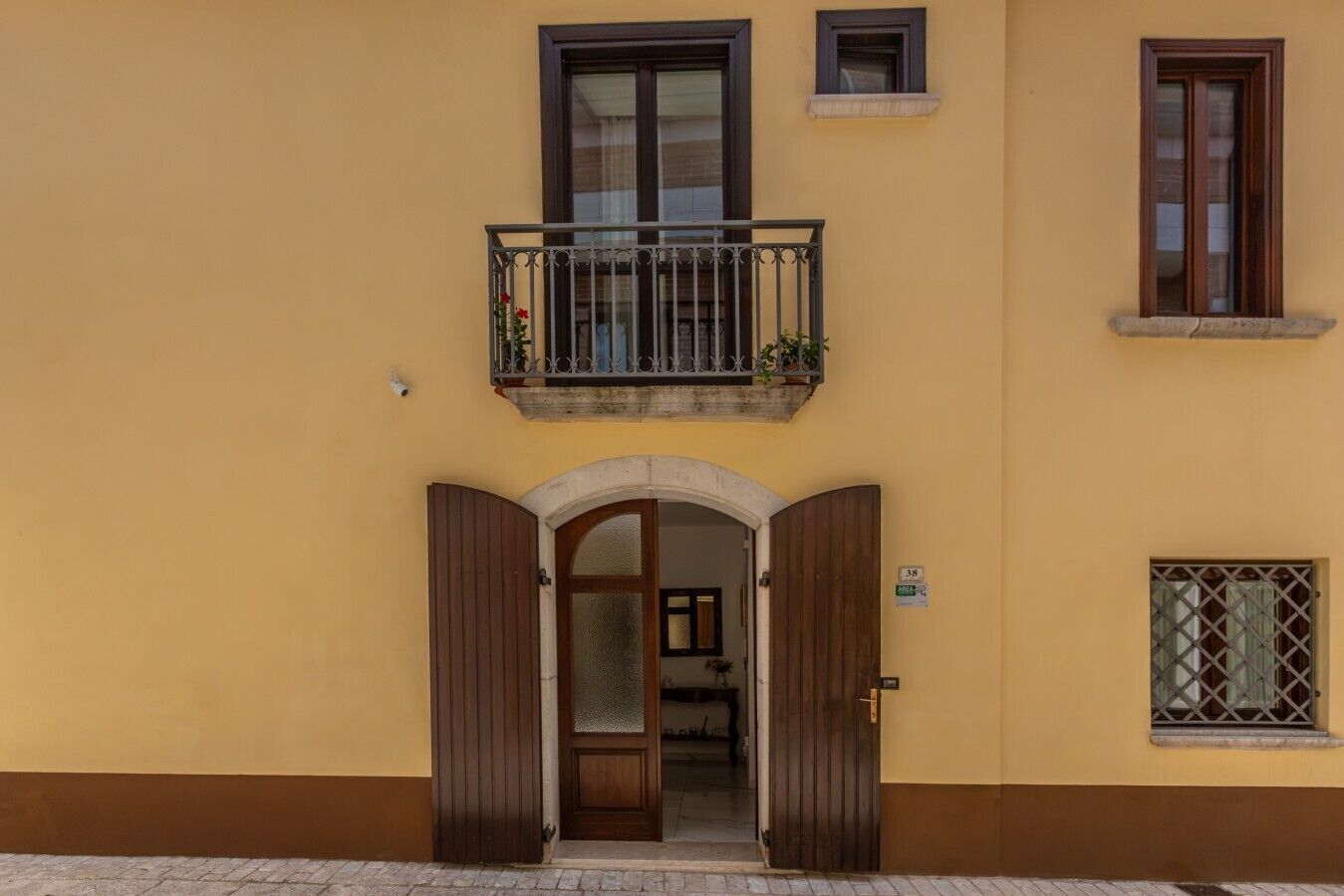 Ein Gebäude mit gelber Fassade, einer Holztür mit Glasfenster und einem Balkon mit Pflanzen.