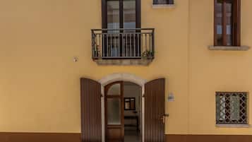 Ein Gebäude mit gelber Fassade, einer Holztür mit Glasfenster und einem Balkon mit Pflanzen.