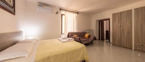 Habitación de hotel con cama, sofá, armario y equipo de aire acondicionado.