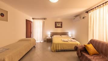 Ein Hotelzimmer mit Doppelbett, Einzelbett, einer Schlafcouch, einem Nachttisch und einer Wandlampe.