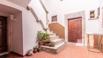 Ein Innenhof mit Terrakotta-Fliesen, einer Holztür, einer Treppe und Kübelpflanzen.
