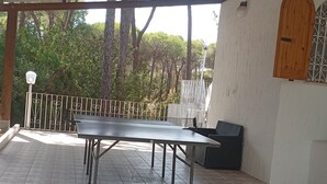Um alpendre coberto ao ar livre com mesa de pingue-pongue, assentos e vista para árvores.