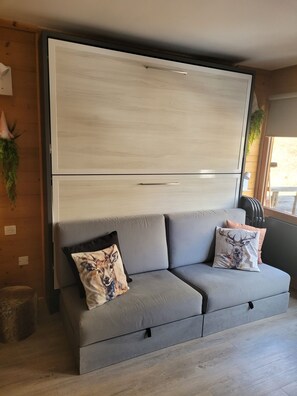A modern living room with a grey sofa, two decorative pillows, a wooden cabinet, and a window with a view. - ✨ The perfect spot at Snow! A charming, fully renovated studio apartment in the heart of Avoriaz, (Avoriaz,Morzine)