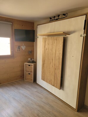 Ein Zimmer mit einem Holzschrank, einem kleinen Tisch mit Körben und einem Fenster mit Jalousien.