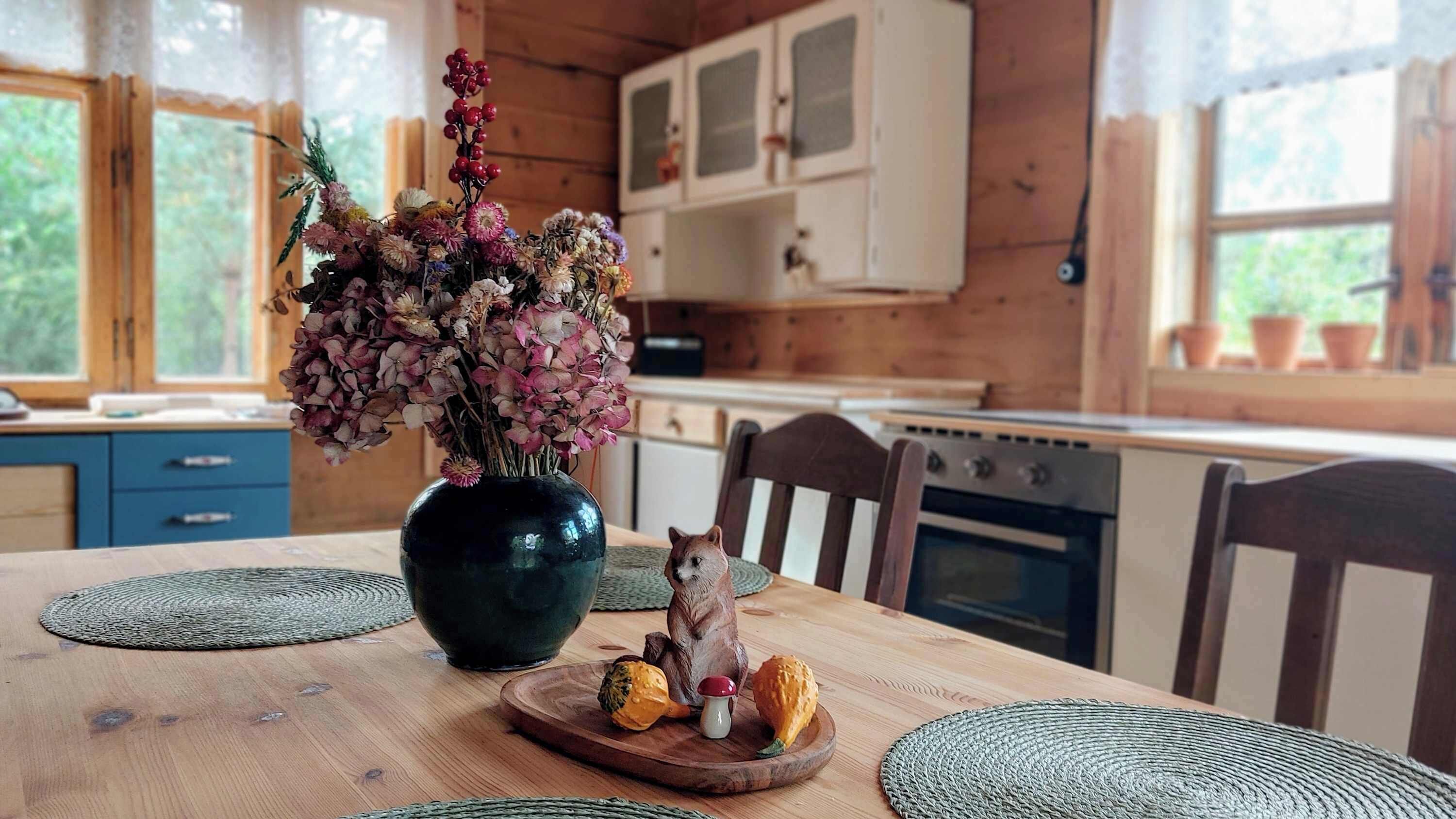 A wooden dining table with a vase of flowers, a ceramic cat figurine, and a wooden board with mushrooms.