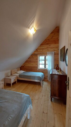 Ein gemütliches Schlafzimmer im Dachgeschoss mit zwei Betten, einer Holzkommode und einem Fenster mit Vorhängen.