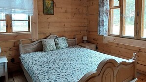 Een slaapkamer in een houten blokhut met een bed, nachtkastje, lamp en raam met gordijnen.