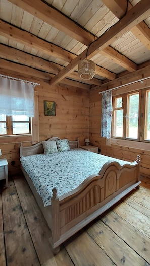 Ein Schlafzimmer einer Holzhütte mit einem Bett, einem Nachttisch, einer Lampe und einem Fenster mit Vorhängen.