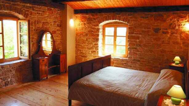 A rustic bedroom with stone walls, a wooden bed, a dresser with a mirror, and two windows with wooden frames. - Villa Morus by Villas Guide (Svetvincenat)