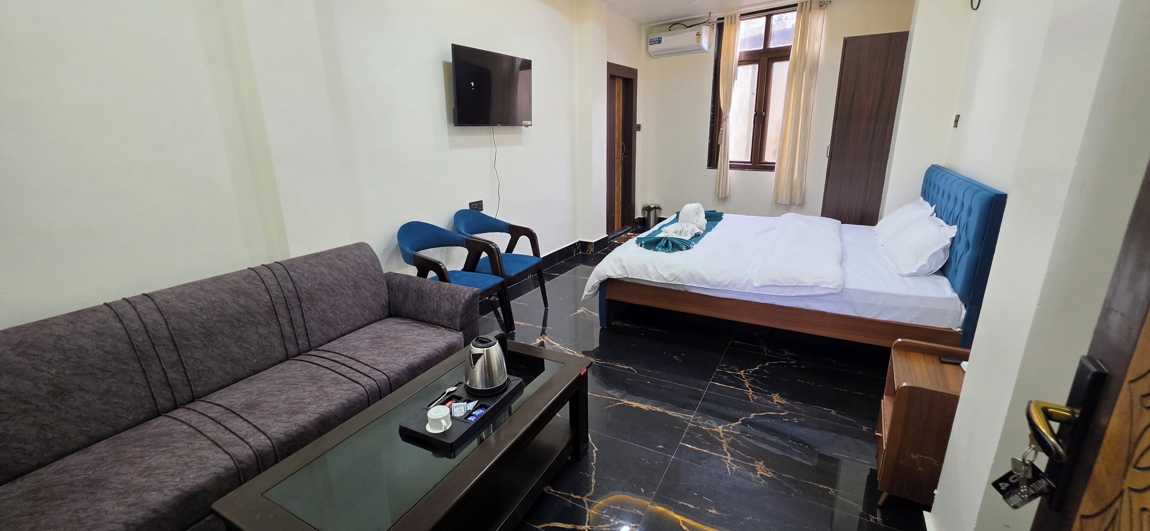 Habitación de hotel pequeña con sofá, cama, una mesita con hervidor de agua y televisión montada en la pared.