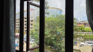 Vista a través de una ventana con cortinas, mostrando una escena urbana con edificios, árboles y coches estacionados.