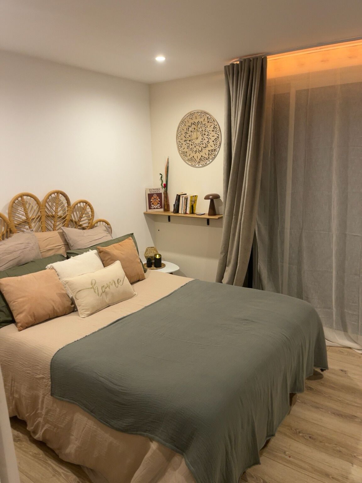 Ein Schlafzimmer mit einem Bett, einem Nachttisch, einem an der Wand befestigten Regal mit Büchern und einem dekorativen Gegenstand sowie einem Vorhang.