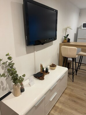 A modern kitchen with a flat-screen TV mounted on the wall, a wooden dining table, and a white countertop with various kitchen items. - A Casarella di Lisa - Cozy studio with a terrace (Vescovato)