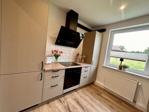 Una cocina moderna con estufa integrada, muebles de cocina blancos y un ventanal con vistas al exterior.