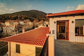 A residential building with a red-tiled roof, a balcony, and a view of a hilly landscape.