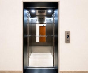An elevator with a metallic interior, a control panel on the right, and a wooden door at the top.