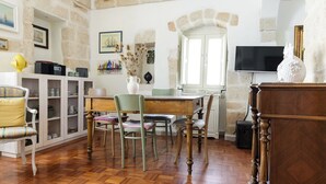 Una habitación con suelo de madera en espiga, una mesa de comedor con sillas, un televisor y una pared de piedra.