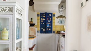 Cocina estrecha con una puerta azul decorada con diversos objetos, un refrigerador blanco y un salpicadero amarillo de azulejos.