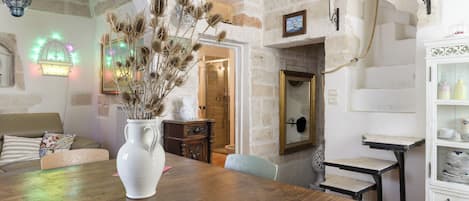 A rustic interior with a wooden table, a white vase with dried plants, and a stone wall.