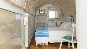 Un dormitorio con techo de piedra, una cama con manta a rayas, una silla y un aparador.