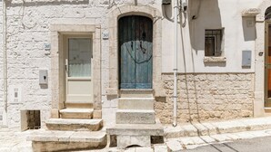 Un edificio con fachada de piedra, una puerta de madera y un conjunto de escalones de piedra que conducen a una puerta con portón metálico.