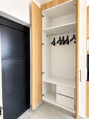 A walk-in closet with a black door, wooden shelving, and a clothing rack. - Aido Studio at Tsavo Fedha | Near JKIA,SGR And EASA. (Nairobi)