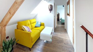 A bright yellow sofa with patterned pillows, a white side table, and a potted plant in a corner. - Gorgeous home in Huisnes sur mer with WiFi (Huisnes sur mer)