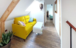 Ein hellgelbes Sofa mit gemusterten Kissen, ein weißer Beistelltisch und eine Topfpflanze in der Ecke.