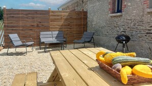 An outdoor patio with wooden furniture, a grill, and a basket of vegetables. - Gorgeous home in Huisnes sur mer with WiFi (Huisnes sur mer)