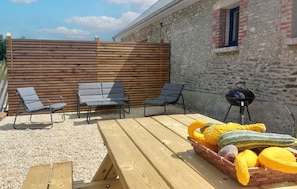 Eine Terrassengruppe mit Holzmöbeln, einem Grill und einem Korb voller Gemüse.