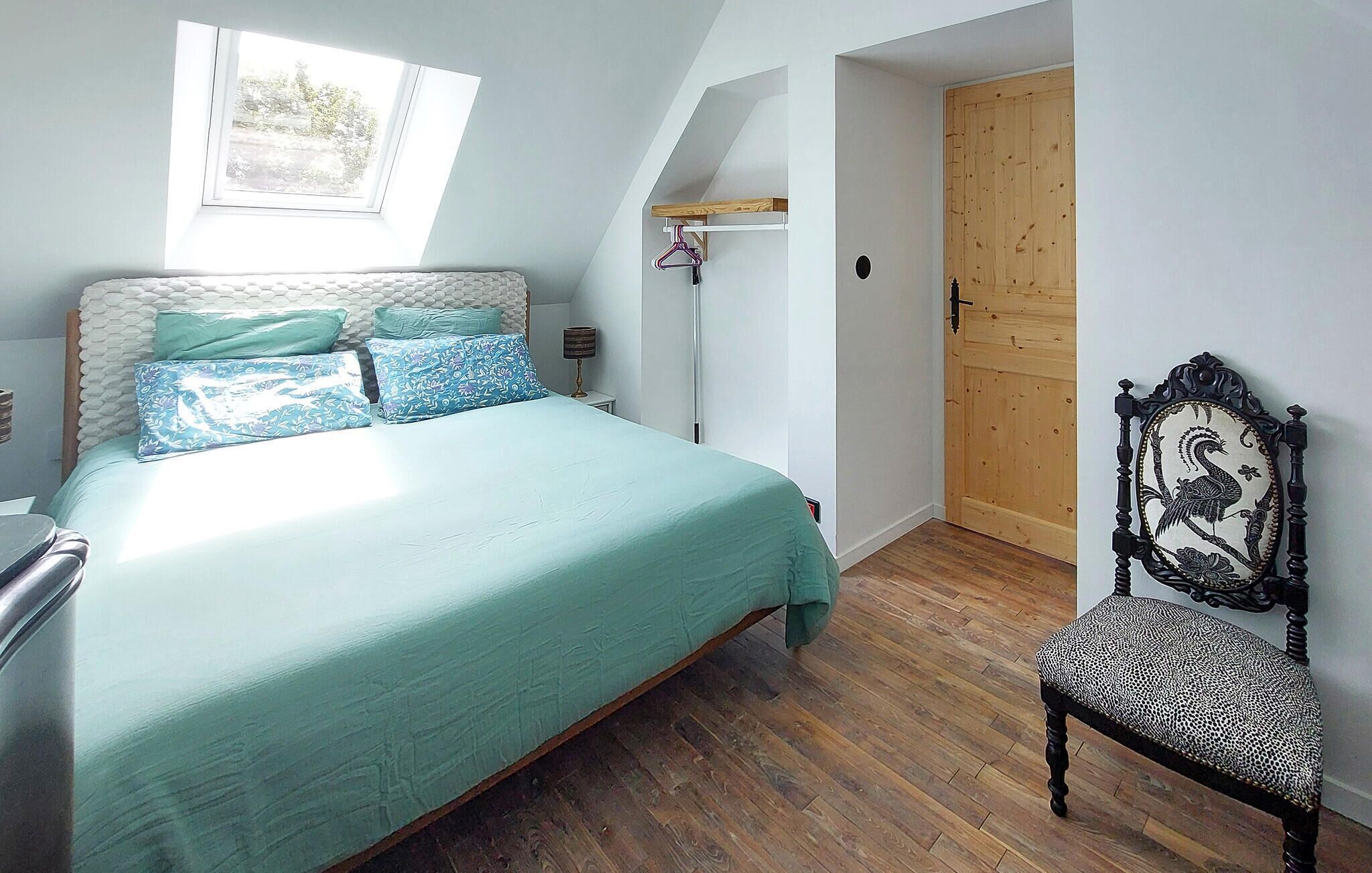 Een slaapkamer met een bed, een stoel, een houten deur en een raam.