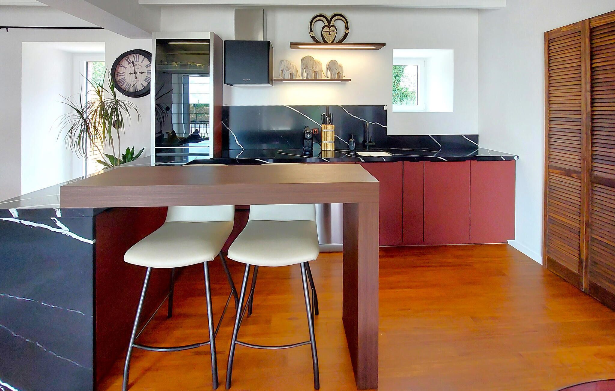 Une cuisine moderne avec un îlot central, des tabourets de bar et une horloge au mur.