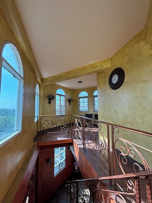 Un interior espacioso con una escalera de madera, ventanas de arco y un reloj en la pared.
