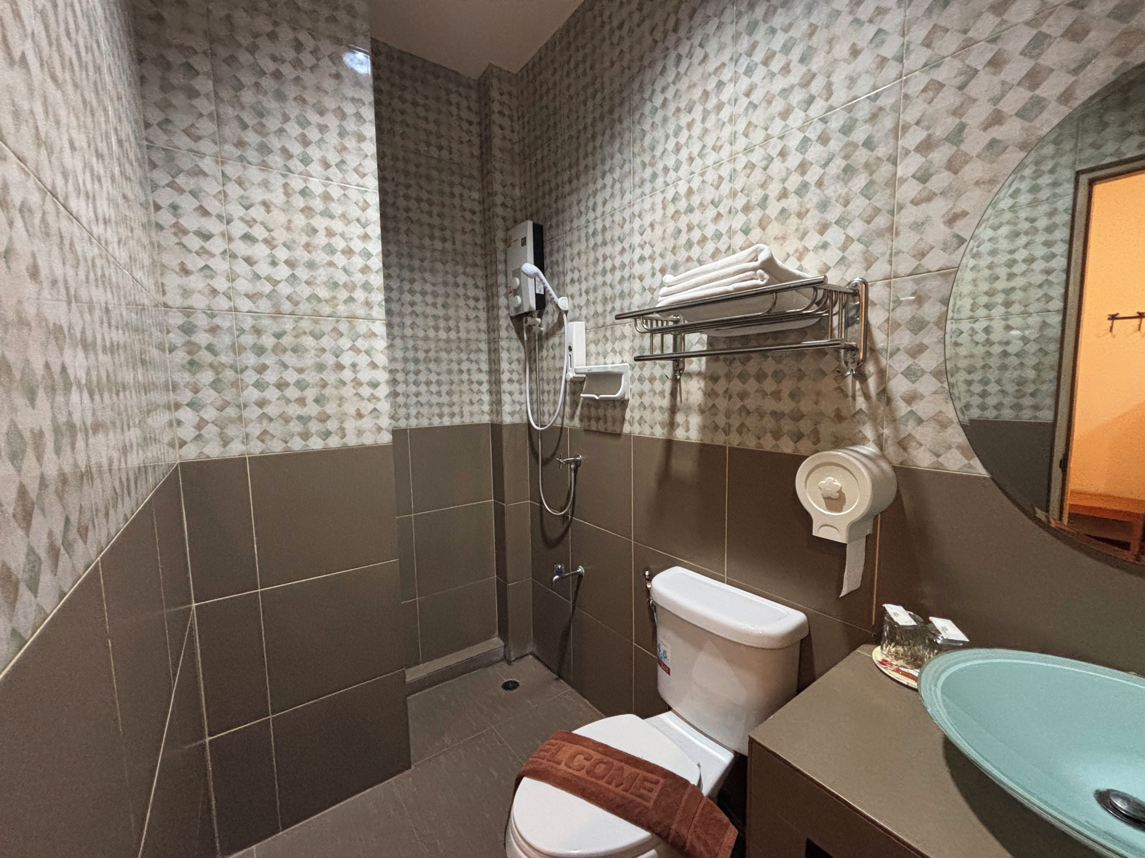 Une salle de bain avec des murs à motifs, des toilettes, un lavabo, un miroir et une douche.