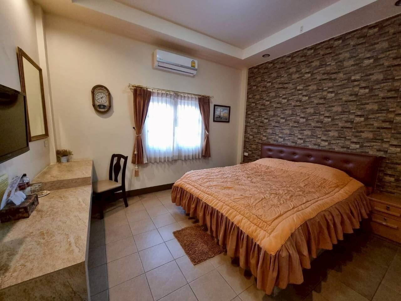 A bedroom with a bed, a desk, a chair, a clock, and a window with curtains.