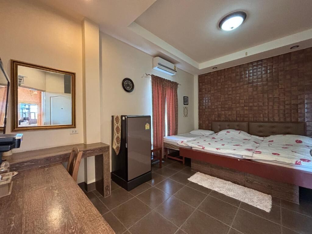 Quarto com cama, uma mesa pequena, frigorífico, espelho e janela com cortinas.