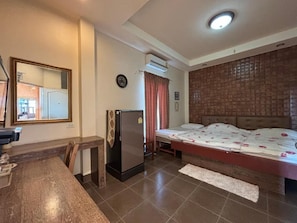 Una habitación con cama, una mesita, un refrigerador, un espejo y una ventana con cortinas.