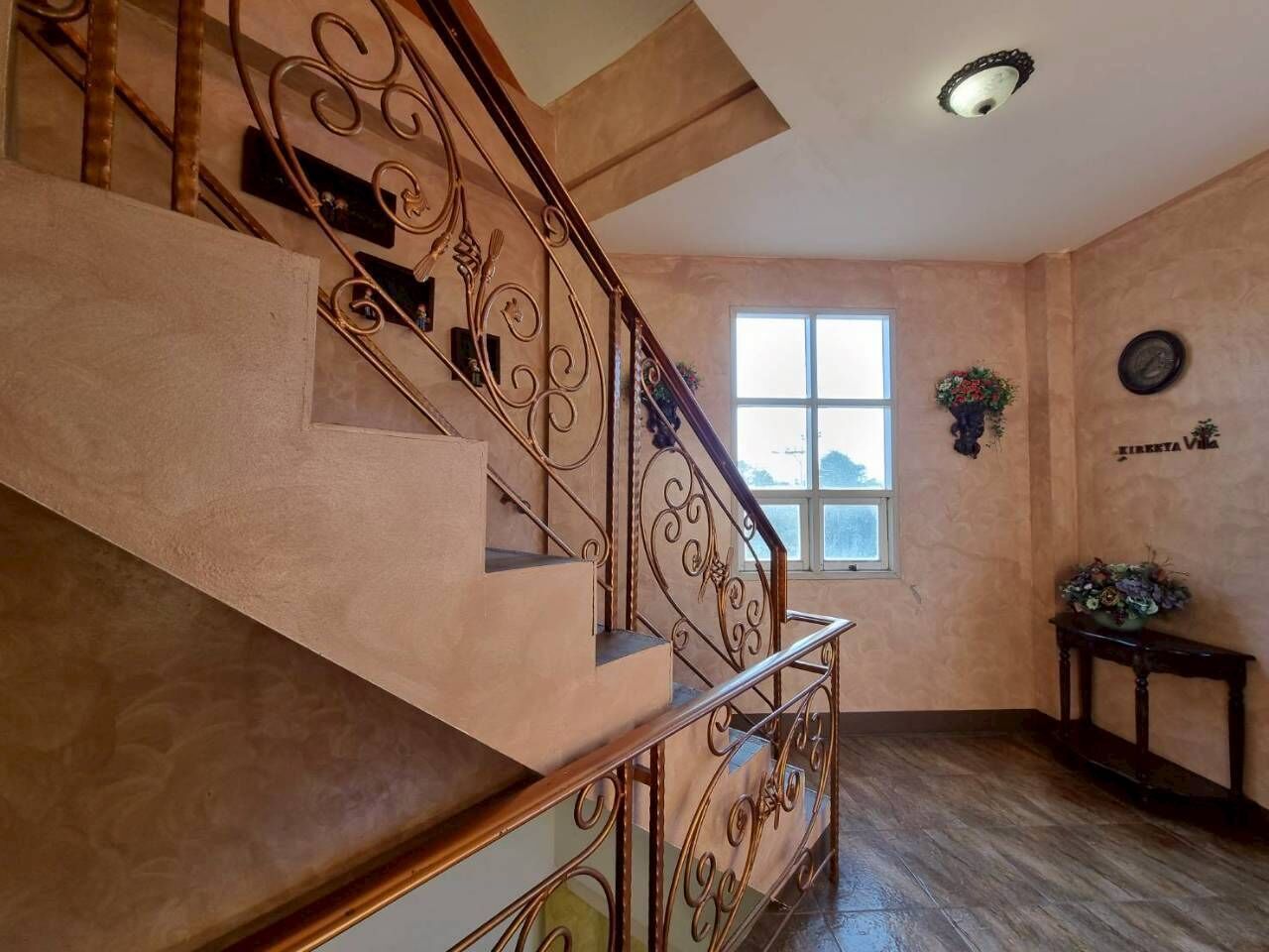 A staircase with ornate metal railings, a wooden handrail, and a wall-mounted clock.