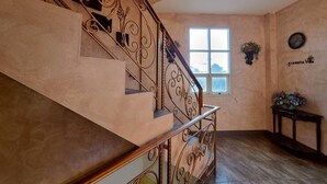 Una escalera con barandillas de metal decorativo, un pasamanos de madera y un reloj fijado a la pared.